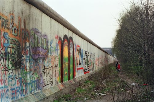 Photograph of the Berlin wall with colourful graffiti and two people in the middle distance