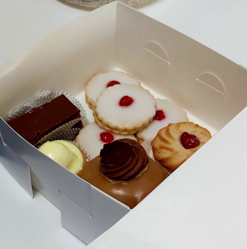 An open box is filled with assorted cakes and biscuits