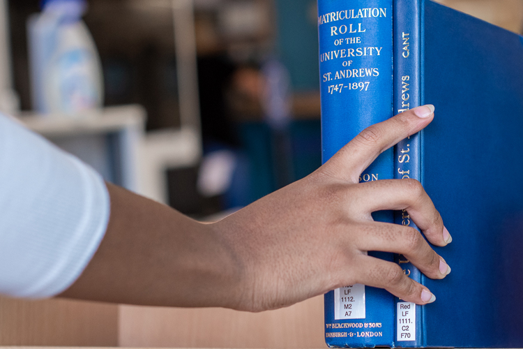 Hand of student is seen reaching to pick up a blue book