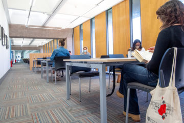 Students sitting at tables in the Main Library. They wear face masks and are socially distant