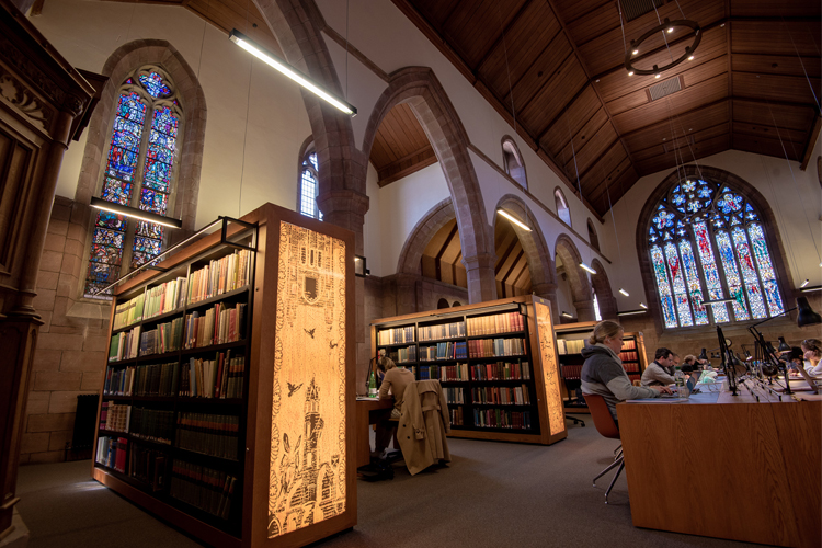 Studying at tables in Thomson Reading Room, illuminated panels and stained-glass windows