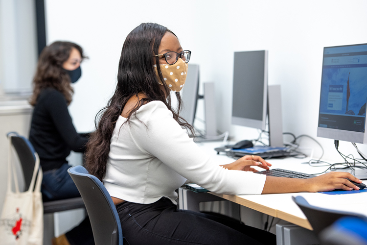 Student working at pc in Main Library wearing face mask