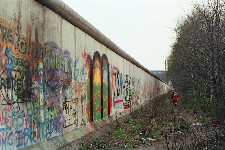 Photograph of the Berlin wall with colourful graffiti and two people in the middle distance