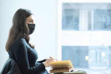 Student sitting at desk with book open, wearing face covering, by window